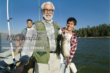 Membres masculins de la famille de trois générations sur le bateau de pêche, homme tenant le poisson