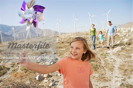 Girl (7-9) with pinwheel standing on wind farm, portrait