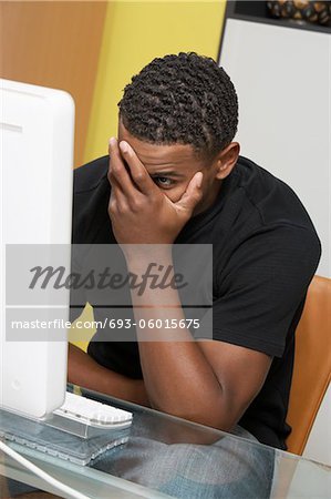 Man covering face with hand sitting at computer