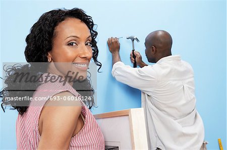 Couple hanging pictures on interior wall, woman smiling, back view