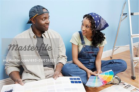 Couple sitting on floor of room looking at paint colour samples
