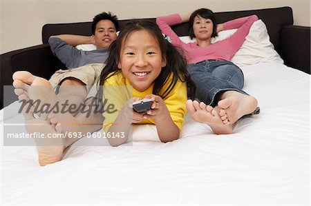 Familie liegend auf dem Bett, Tochter (7-9) zeigenden Fernbedienung, portrait
