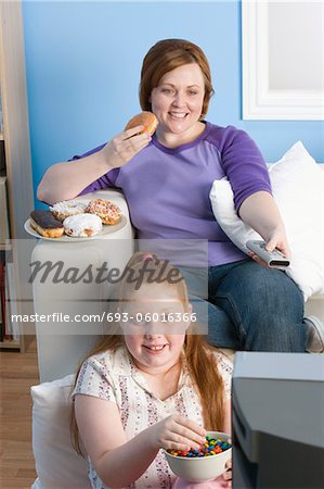 Übergewichtige Mädchen und Mutter vor dem Fernseher, Essen