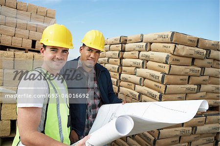 Bauarbeiter stehen in der Nähe von Lieferungen, Schutzhelme tragen, Blick auf Plan vor Ort