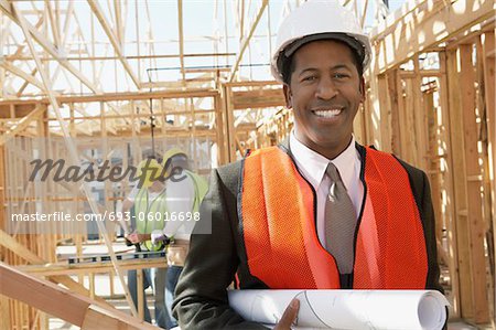 Smiling Surveyor in hard hat with building plans on Construction Site