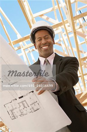 Smiling Surveyor in hard hat with building plans on Construction Site, low angle view