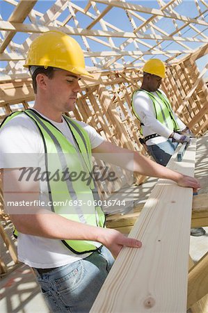 Two construction workers measuring wooden plank