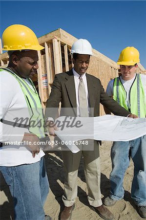 Two construction workers and surveyor studying blueprint