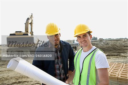 Construction workers with blueprints on site, portrait