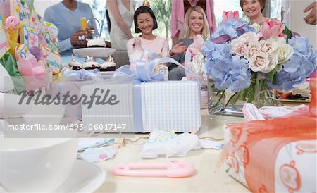 Freunde auf Baby-Dusche sitzen hinter Geschenke und Blumen