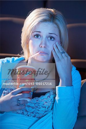 Jeune femme assise au théâtre, boire des boissons gazeuses, main sur la joue, regarder film triste