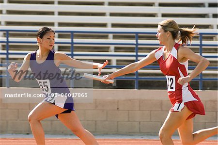 Female track athlete passing relay baton to another one