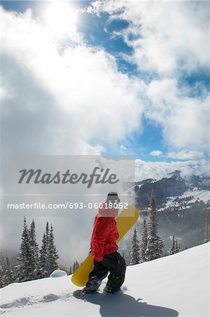 Teenage boy (16-19) holding snowboard, hiking up snow covered slope, full length