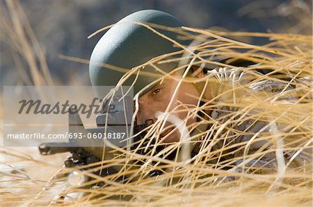 Soldier aiming rifle, hiding in long grass, (close-up)
