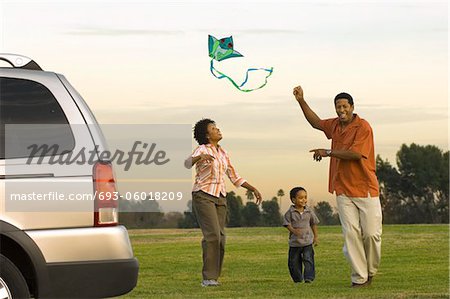 Couple and young son flying kite by car in park