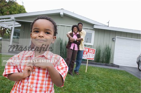 Portrait de garçon (5-6) devant la nouvelle maison, parents en arrière-plan