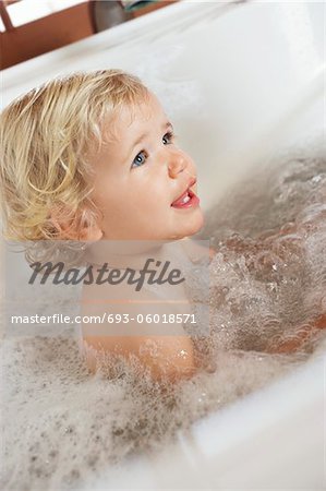 Bébé garçon assis dans une baignoire remplie de bulles, vue latérale