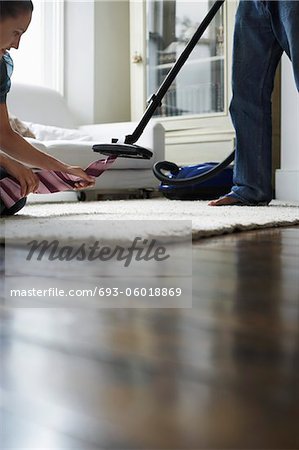 Woman pulling tie from vacuum cleaner in bedroom