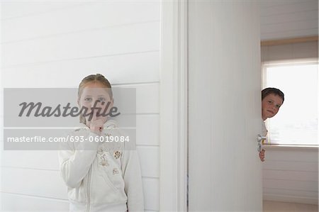 Girl with finger on lips standing by boy peeking round door
