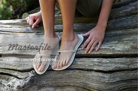 Teenage girl (16-17 years) wearing flip-flops sitting on tree trunk, low  section - Foto de stock - Masterfile - Royalty Free Premium, Número:  693-06019098