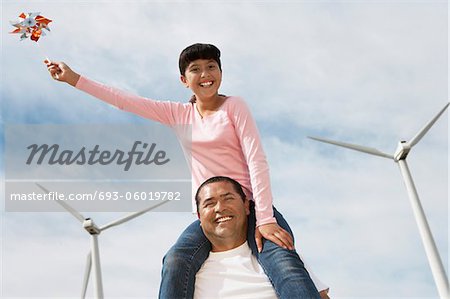 Girl (7-9) sitting on fathers shoulders at wind farm, portrait