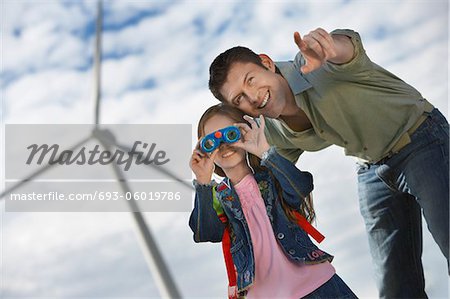 Girl (5-6) using binoculars with father at wind farm