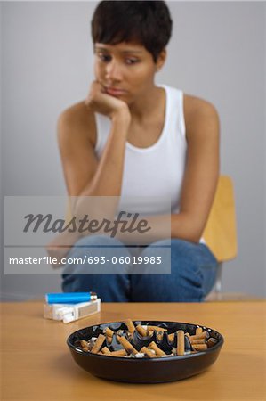 Woman staring at full ashtray of cigarettes on table