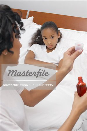 Nurse pouring medication for girl (7-9) lying in bed