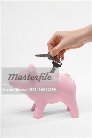 Hand Putting Car Keys in Piggy Bank