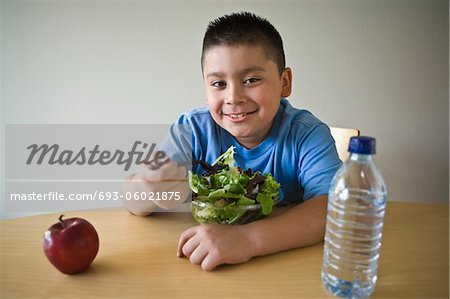 Pre-Teen (10-12) junge am Schreibtisch sitzen und essen Salat