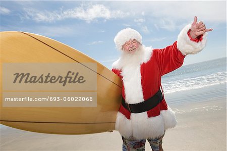 Father Christmas stands with a surfboard at the beach