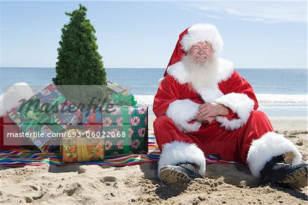 Père Noël se situe sur la plage avec un arbre et présente