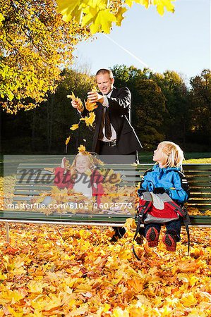Father and children playing with autumn leaves in park