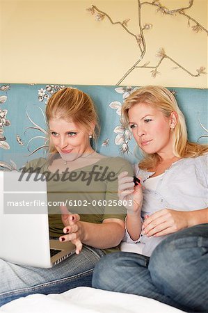 Two young women using laptop in bedroom