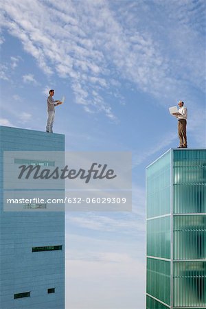 Men standing on top of high rise buildings, using laptop computers