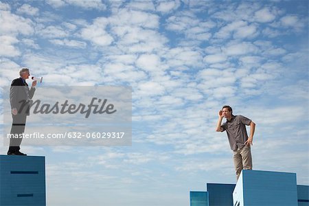 Oversized men standing on rooftops, one speaking through megaphone