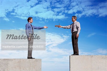 Businessmen standing on platforms, one handing the other a tiny factory