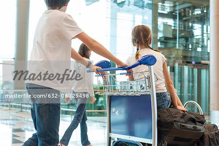 Frères et sœurs, poussant un chariot de bagages dans l'aéroport