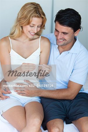 Couple looking at pregnancy test, man with hand on woman's abdomen