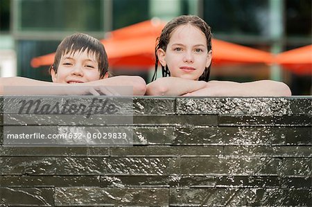 Bruder und Schwester gelehnt am Rand des Swimmingpools nebeneinander