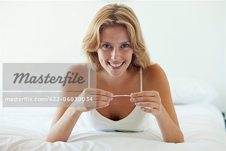 Young woman lying on bed holding pregnancy test