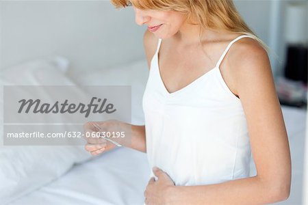 Woman holding pregnancy test on bed, smiling