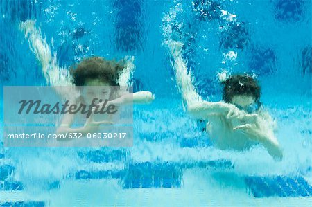 Brother and sister swimming underwater in swimming pool, hands forming finger frames
