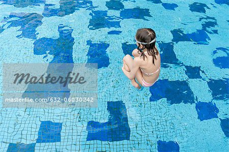 Girl jumping into swimming pool, rear view