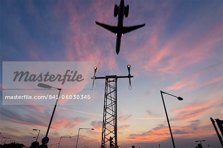 Aéronefs DC9 approchant sur la piste d'atterrissage portiques légers au coucher du soleil, Londres, Royaume-Uni, Europe