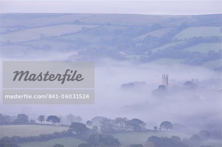 Morning mist swirls around the church tower of Widecombe in the Moor village on Dartmoor, Devon, England, United Kingdom, Europe