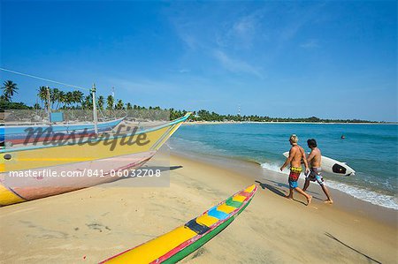 Surfeurs et des bateaux de pêche sur cette plage de surf populaire, durement touchée par le tsunami de 2004, Arugam Bay, Province orientale, Sri Lanka, Asie