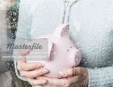 Woman with piggy bank at rainy window