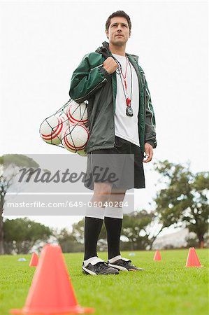 Coach carrying soccer balls on pitch