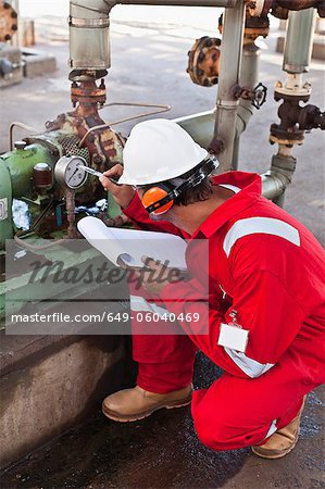 Worker noting gauge at oil refinery